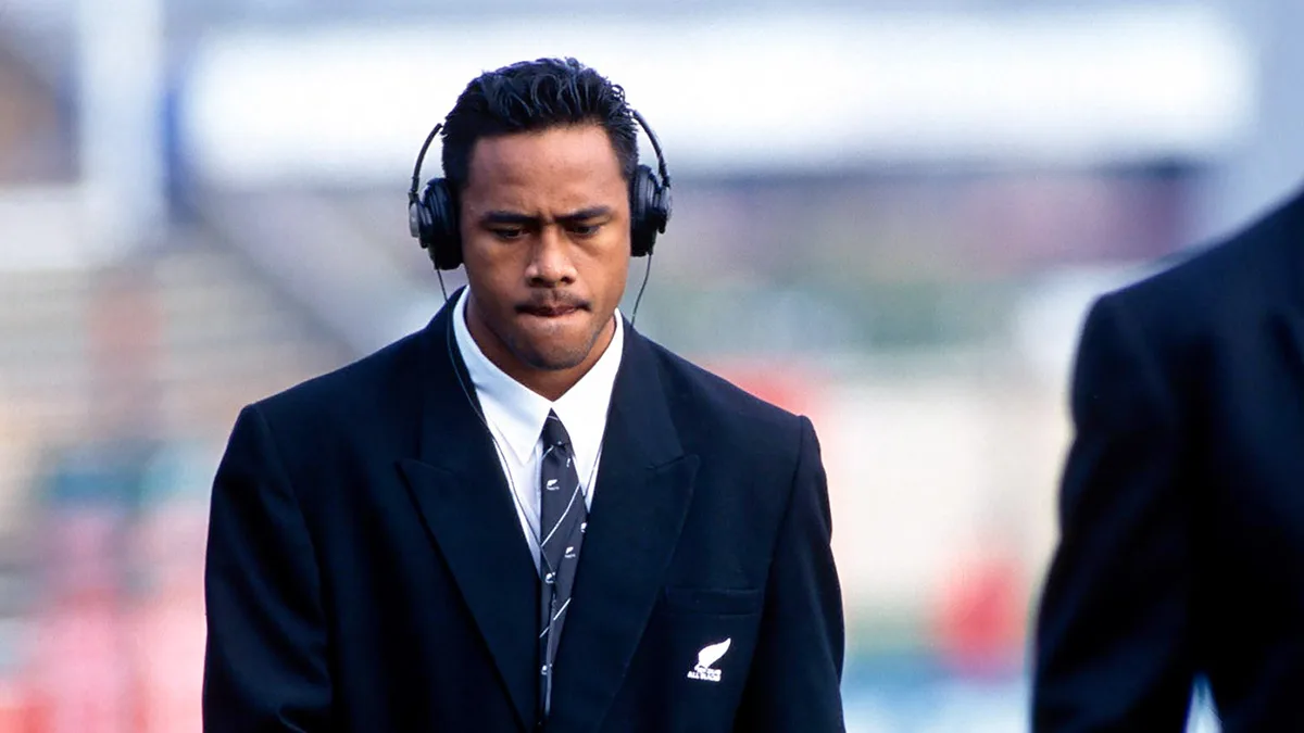 Jonah Lomu in an All Blacks suit and headphones, looking down in concentration